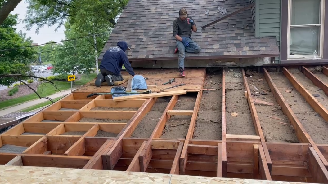 Two roofers removing old shingles, revealing wooden roof structure.