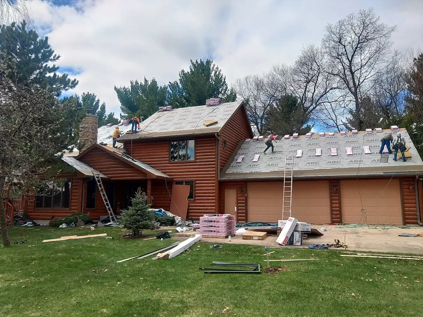 Log cabin house with roof in the process of being replaced; workers on roof.