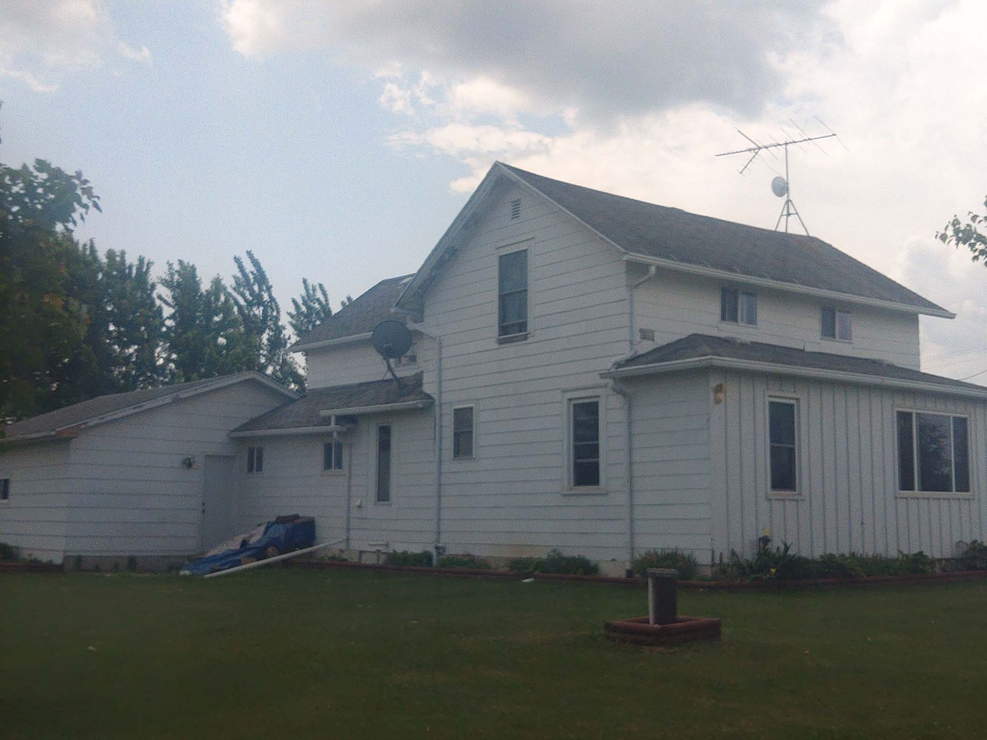 White two-story house with satellite dishes on a green lawn under a cloudy sky.