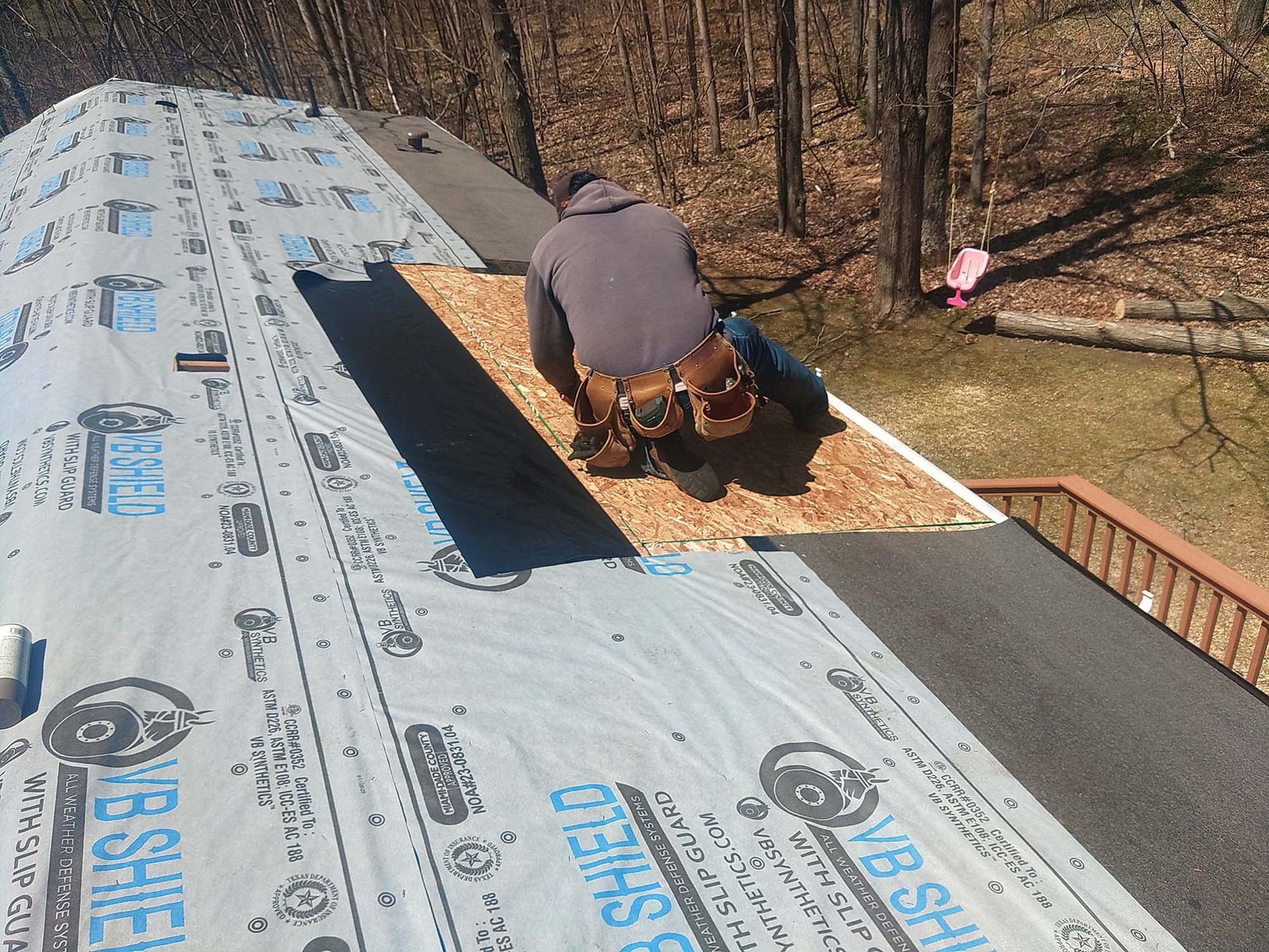 Roofer on a sloped roof replacing wooden shingles. Wearing a work belt, surrounded by construction materials.