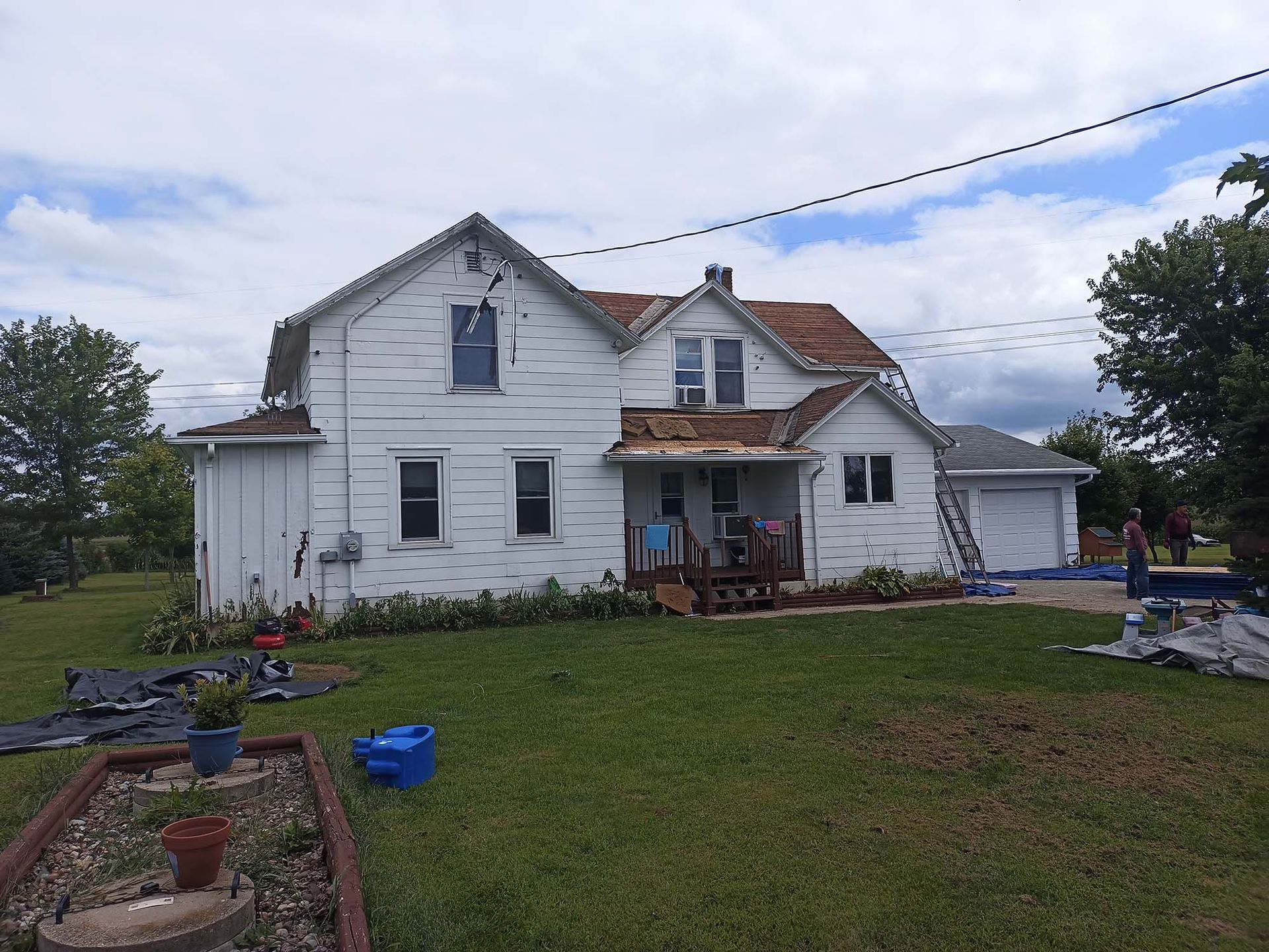 White two-story house with a brown roof under construction, on a grassy lawn with a cloudy sky.