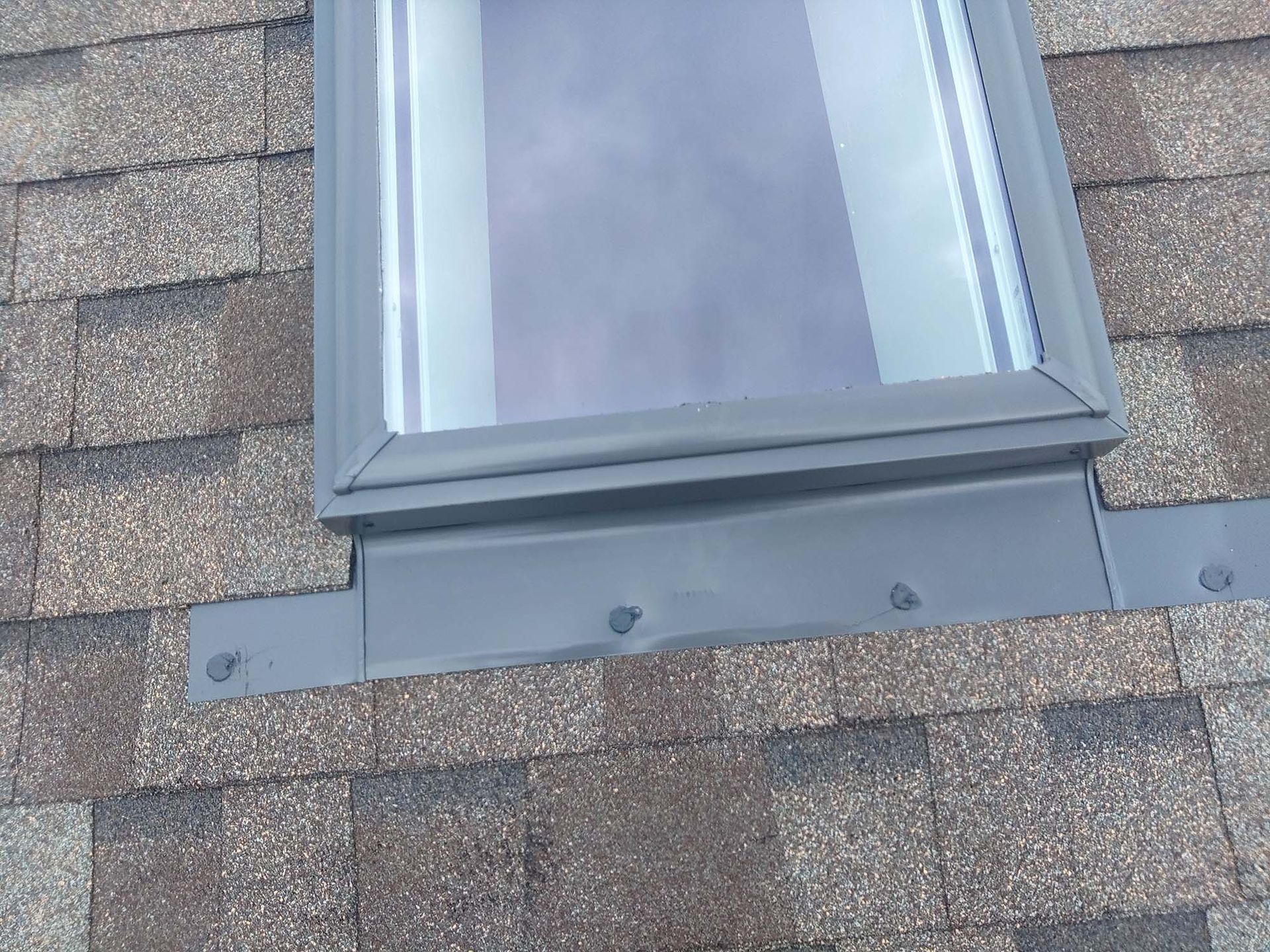 Skylight on a brown shingled roof with a dark gray metal flashing.