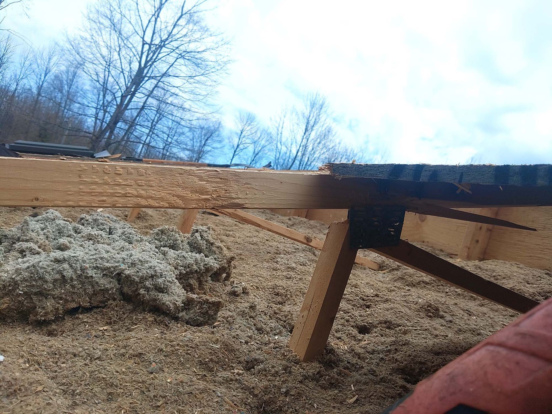 Close-up of a wooden structure with wood shavings and insulation. The sky is visible in the background.