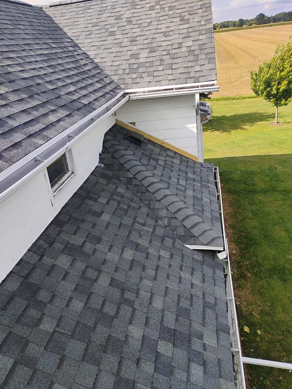 Gray shingled roof with a white fascia and a view of a field.