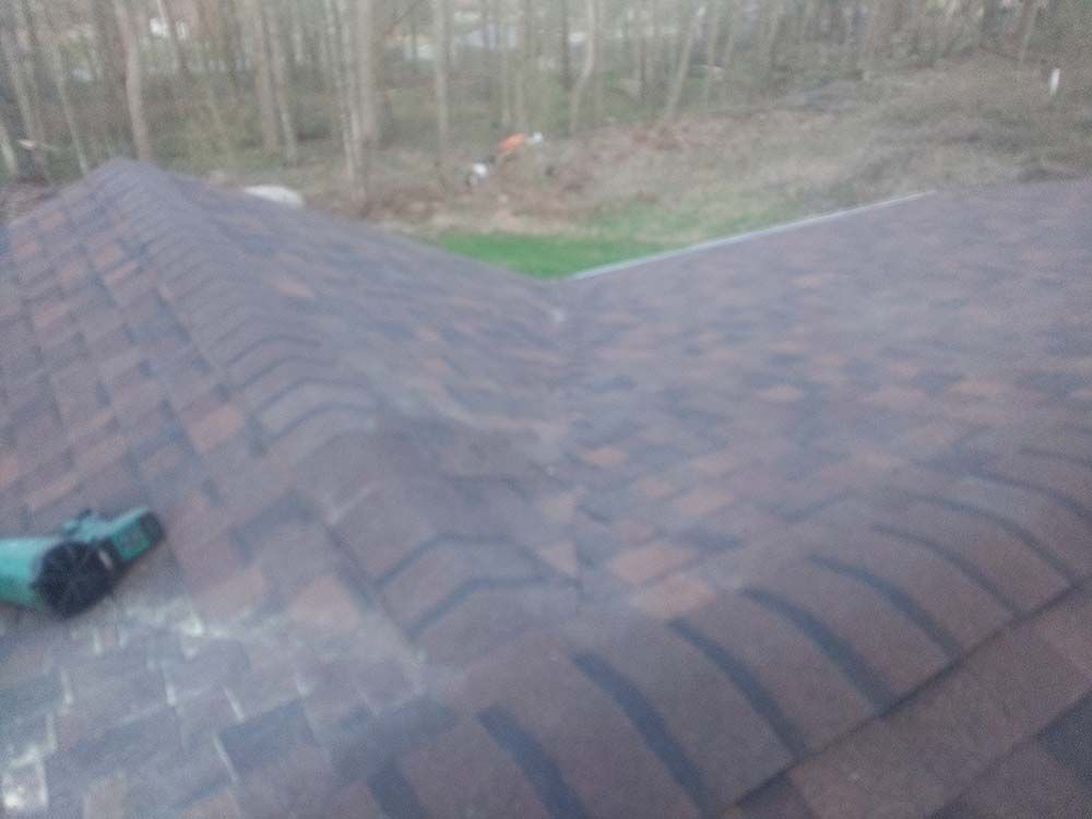 Brown asphalt shingle roof with a valley, trees in the background, and a power tool in the corner.