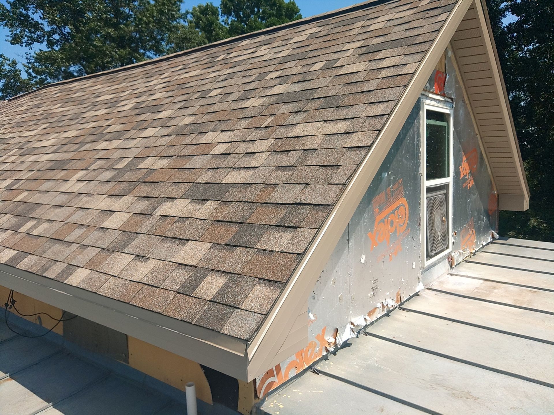 Roof with asphalt shingles and a small window on a gabled section of a house.