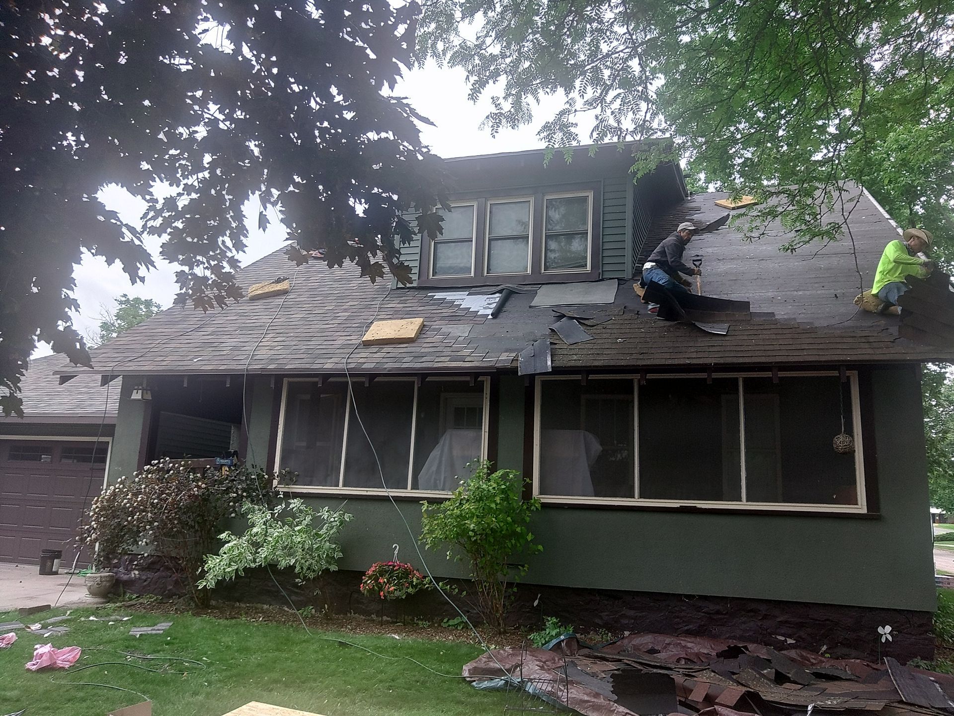 Roofers working on a house with damaged roofing shingles; overcast day.