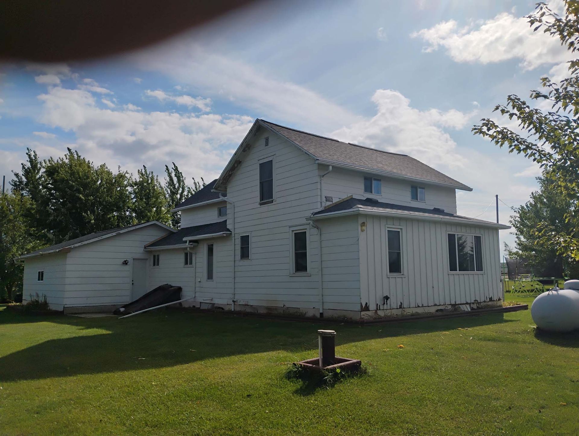 White two-story house with detached outbuilding, set on a grassy lawn with a blue sky background.