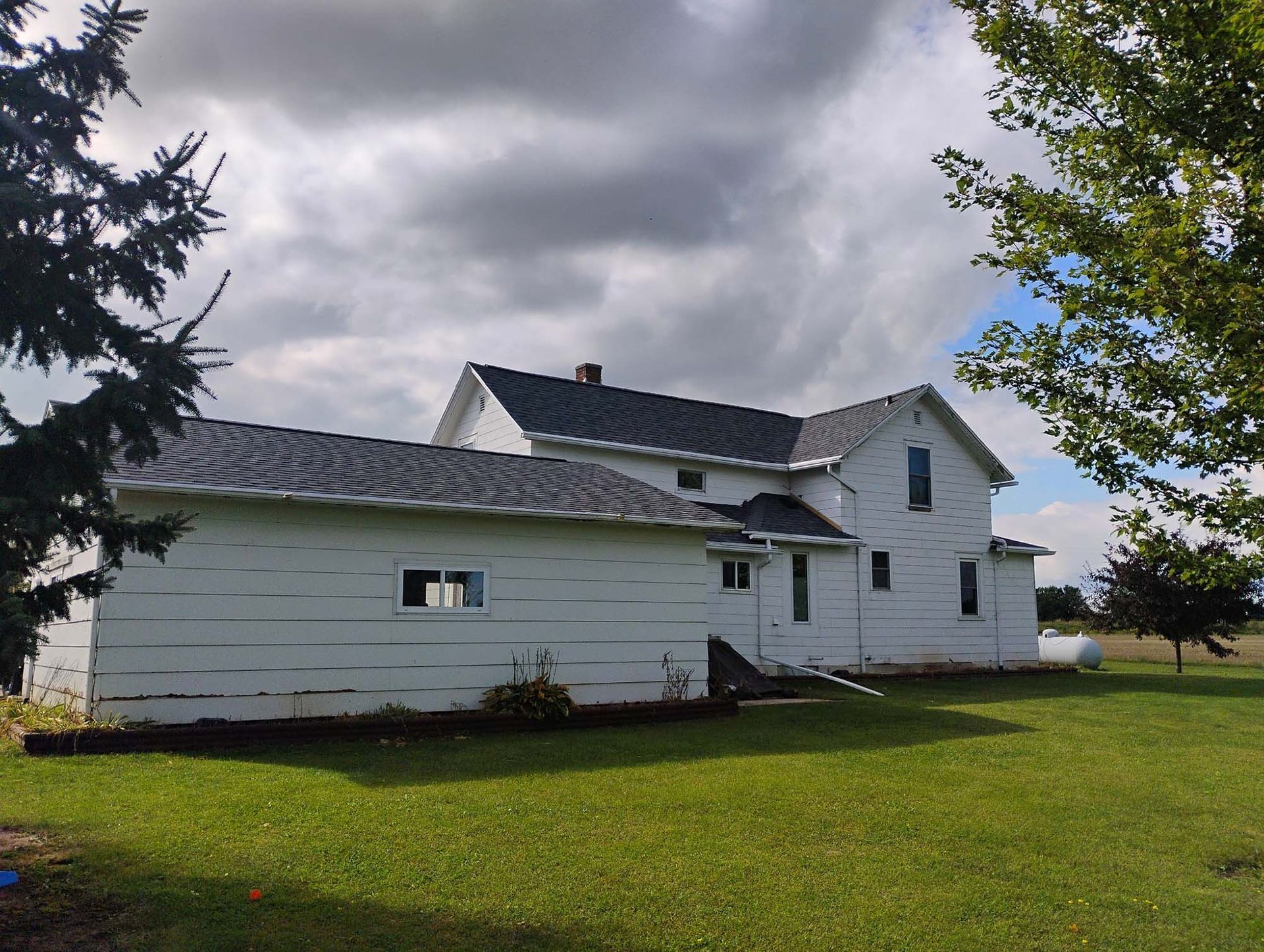 White two-story house with detached garage on a grassy hill under a cloudy sky.