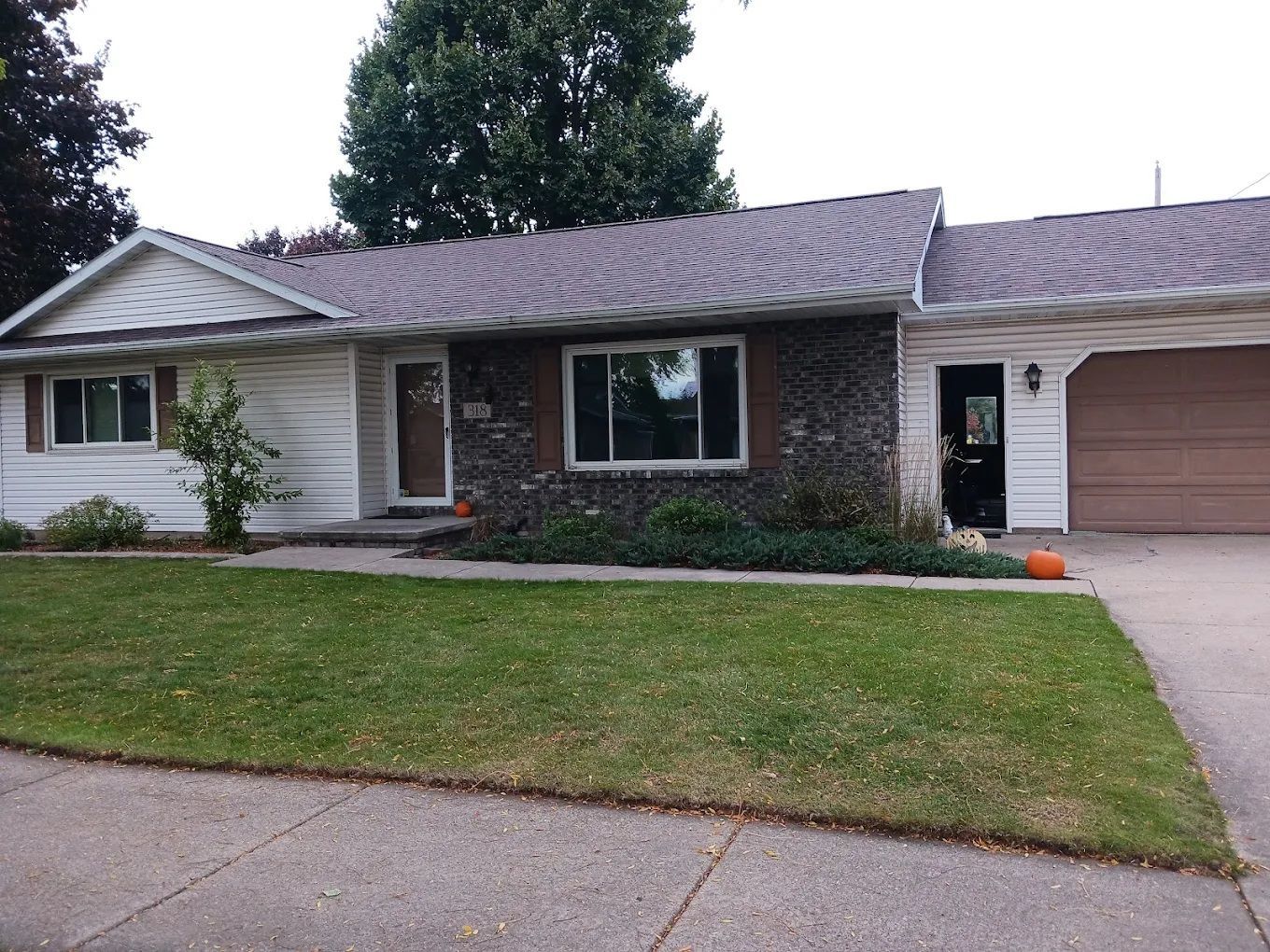 Ranch-style house with white siding, brick facade, brown garage door, and green lawn.