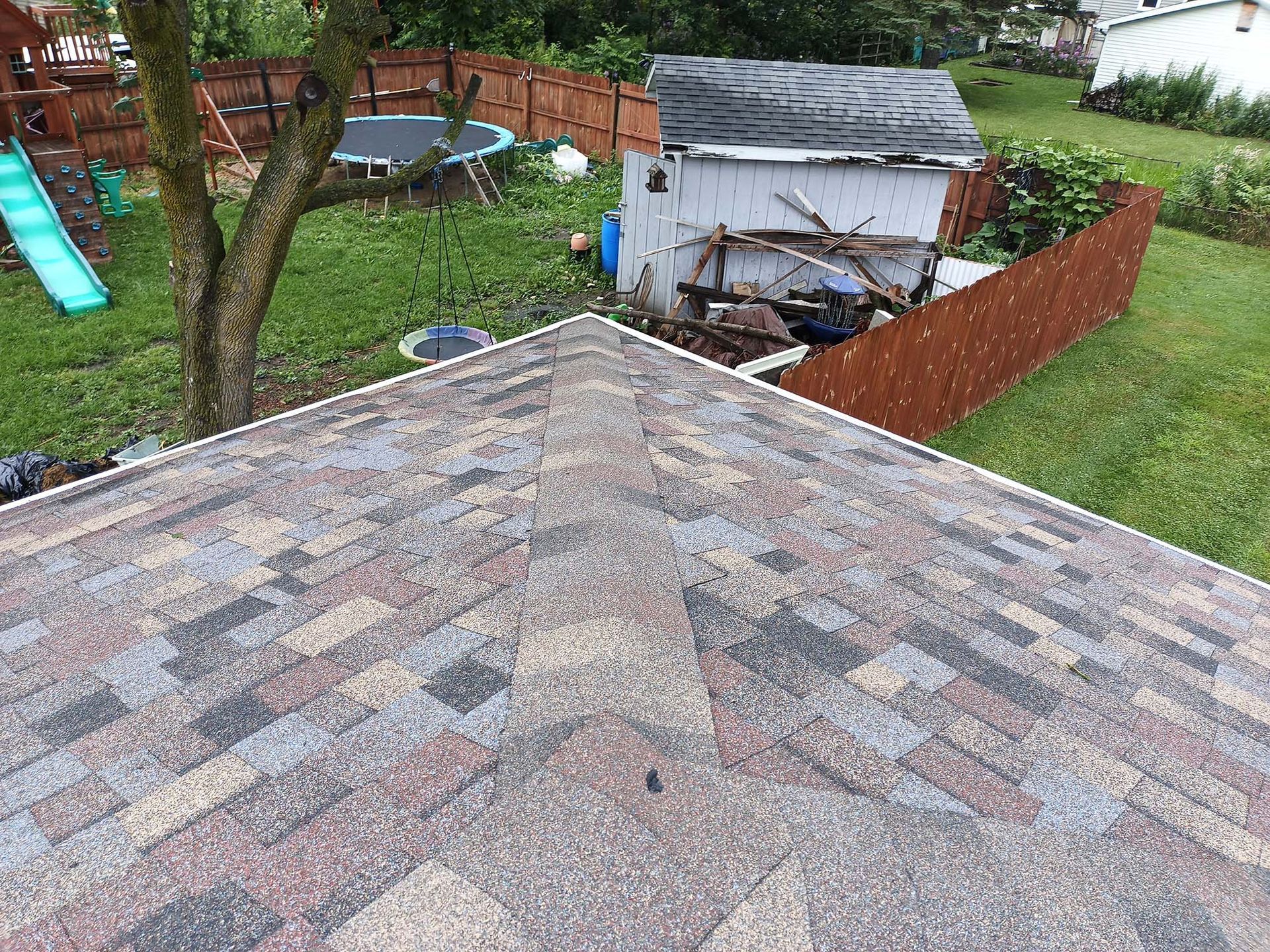View of a shingled roof with a shed and backyard visible in the background.