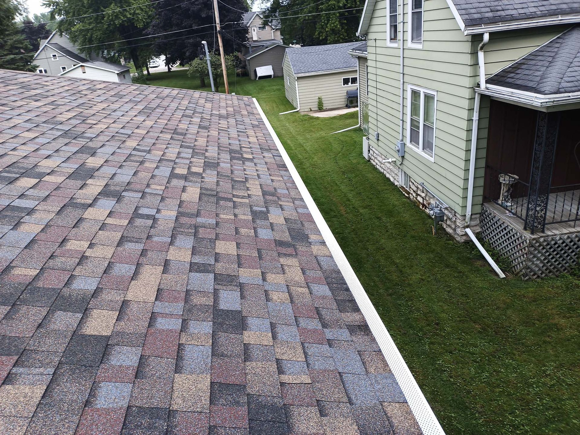 Overhead view of a roof with colorful shingles, next to a green-sided house and green lawn.