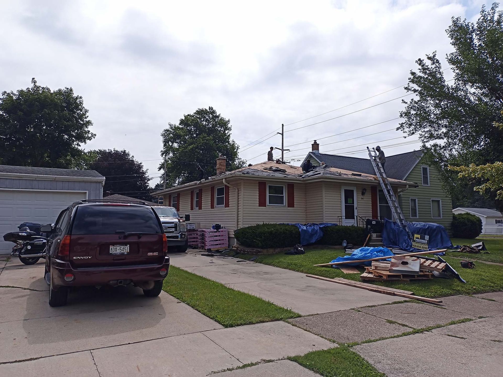 A house with its roof partially removed, construction materials in the yard, cars in the driveway.
