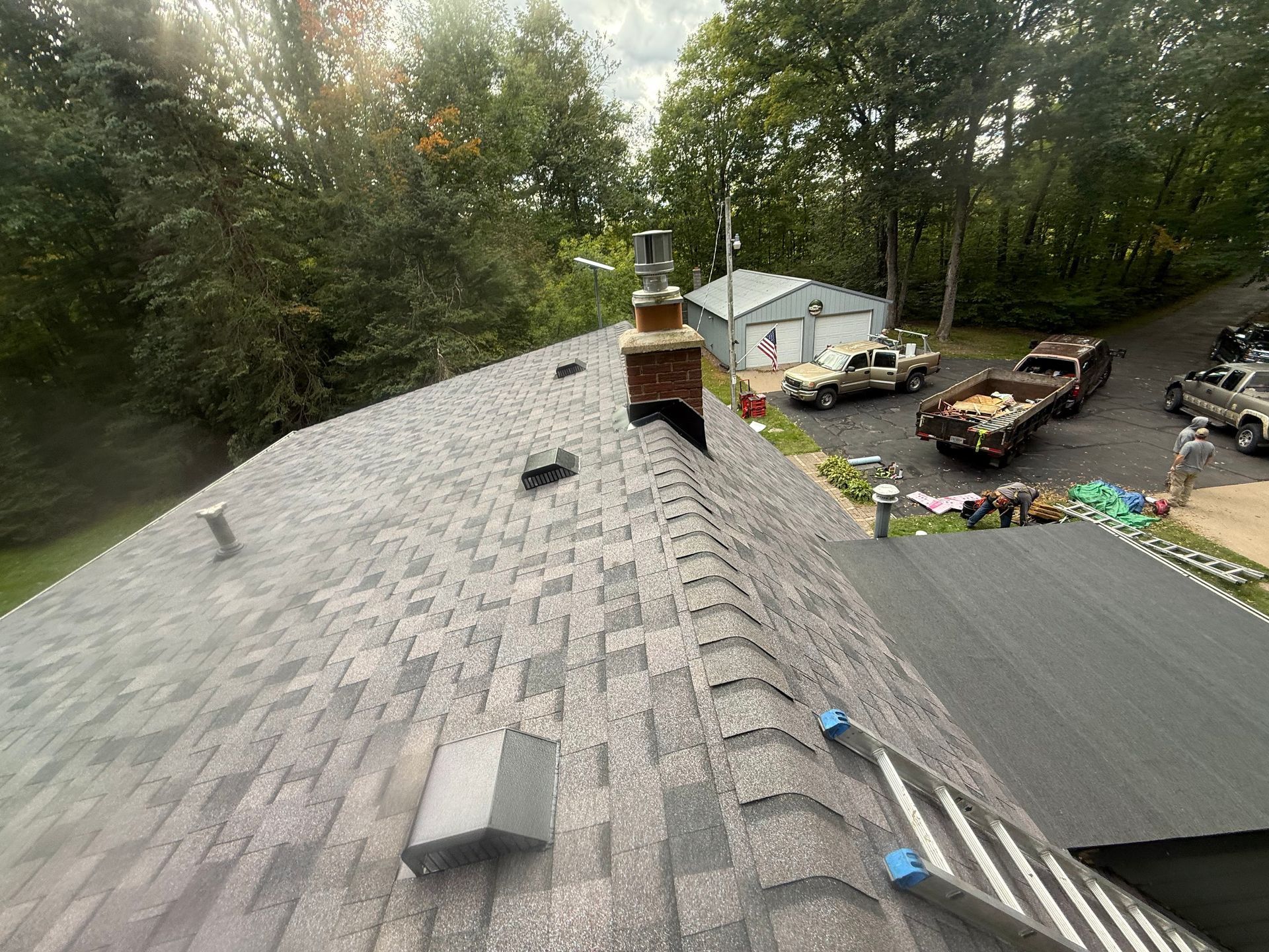 Rooftop view of house with chimney, gray shingles, and construction trucks in the yard.