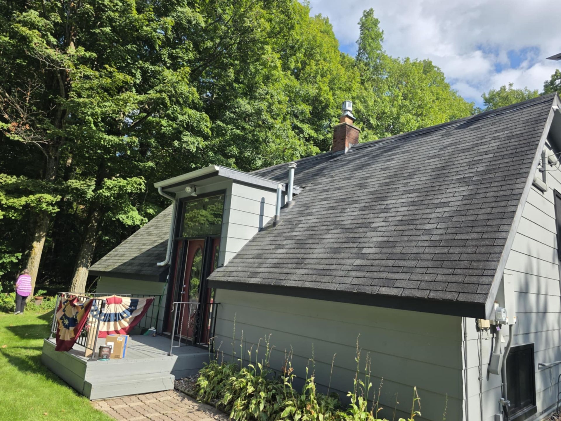 Gray house with a dark roof and large glass windows surrounded by green trees.