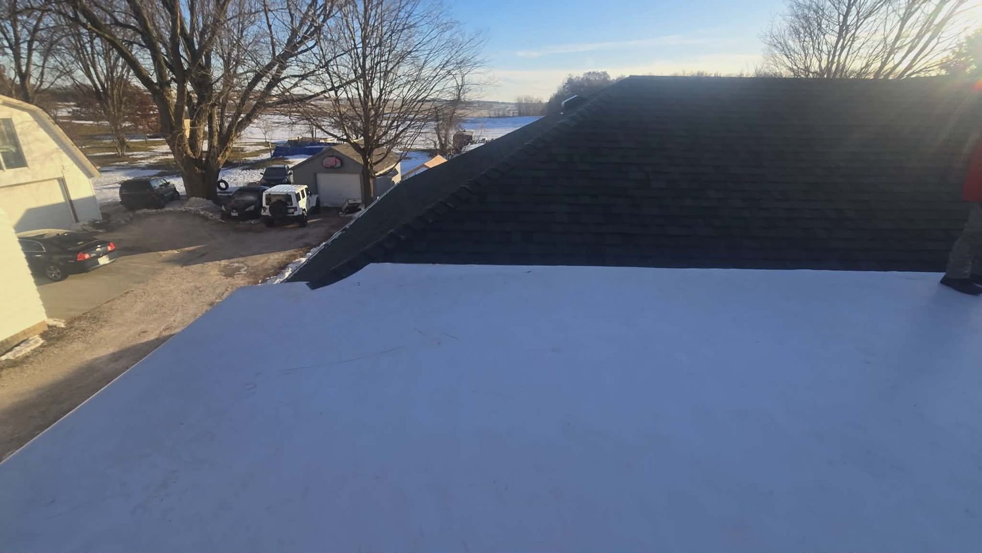 White flat roof with dark shingled roof in background on a sunny day.