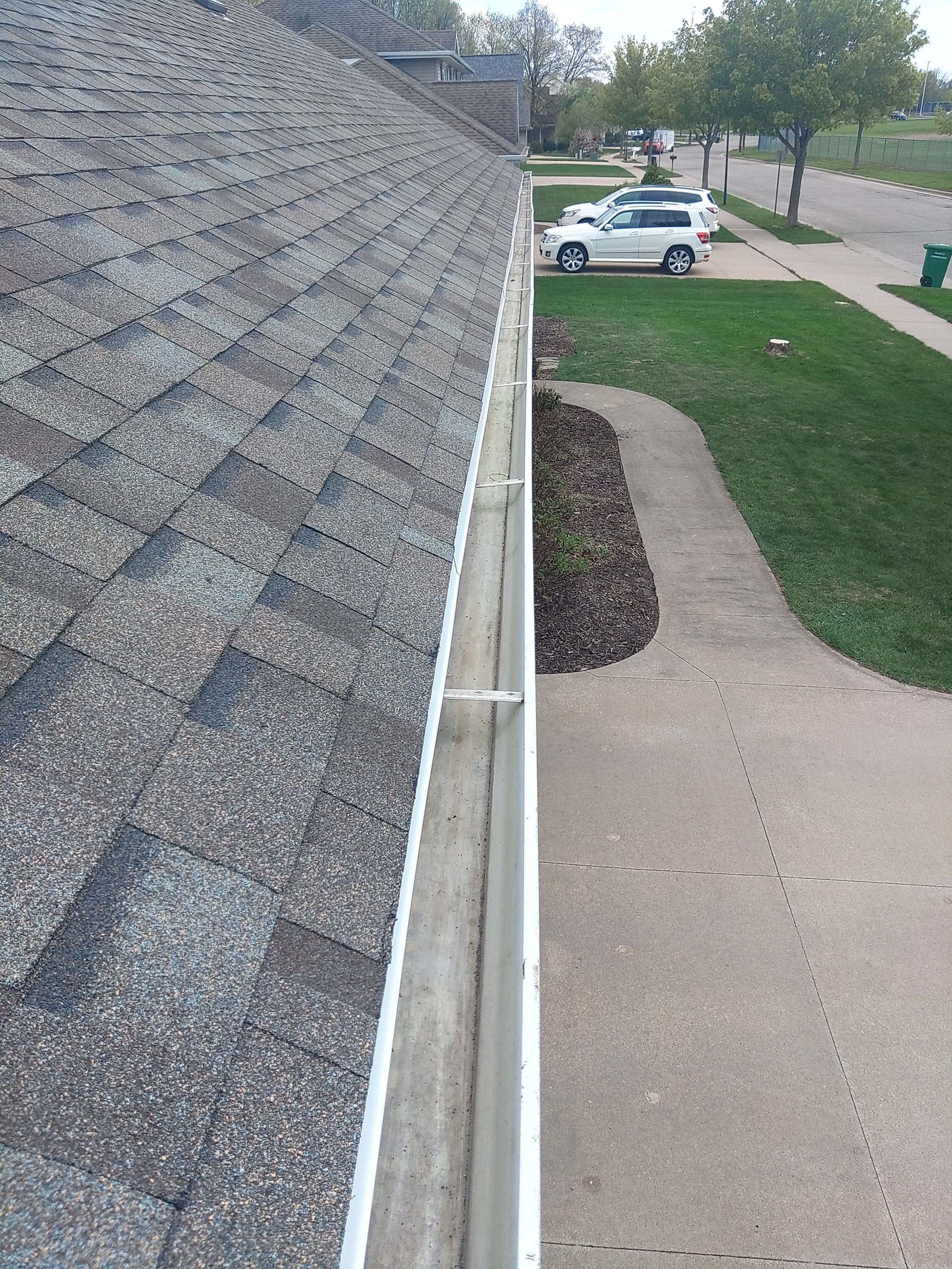 View of a house roof with a gutter and a walkway, a car, and green grass.