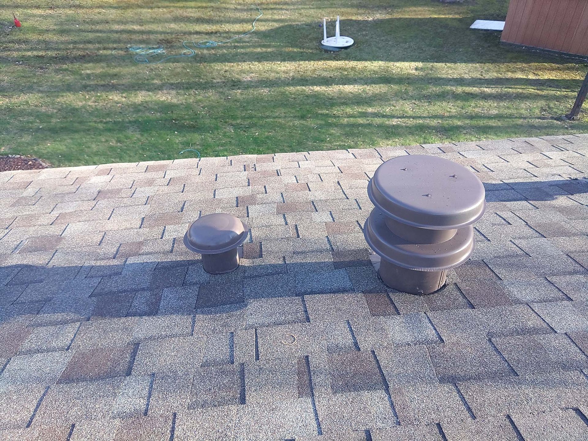 Two brown roof vents on a shingled roof, with green grass in the background.