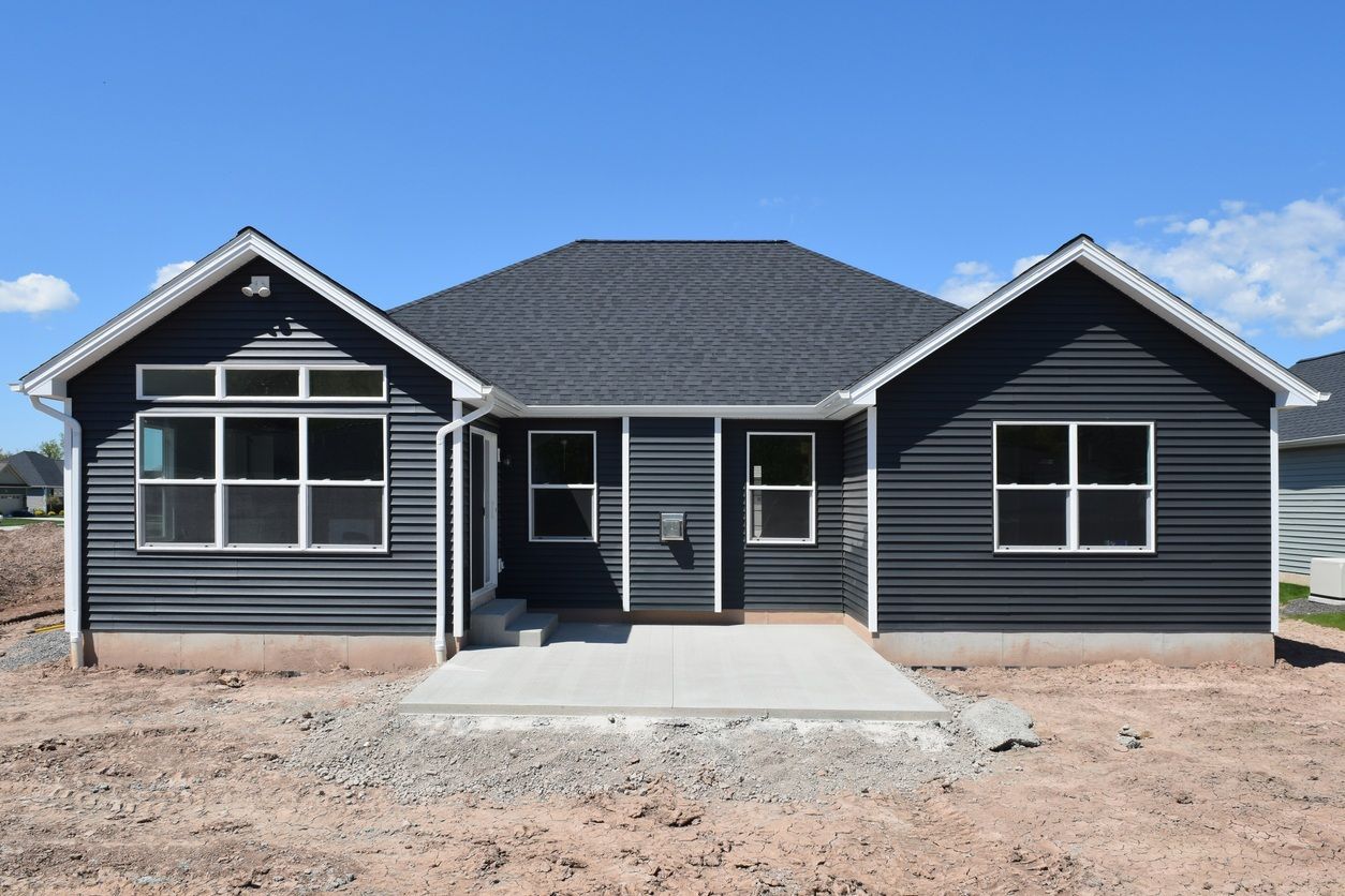 Back exterior of a dark gray house with white trim, featuring a patio and windows against a blue sky.