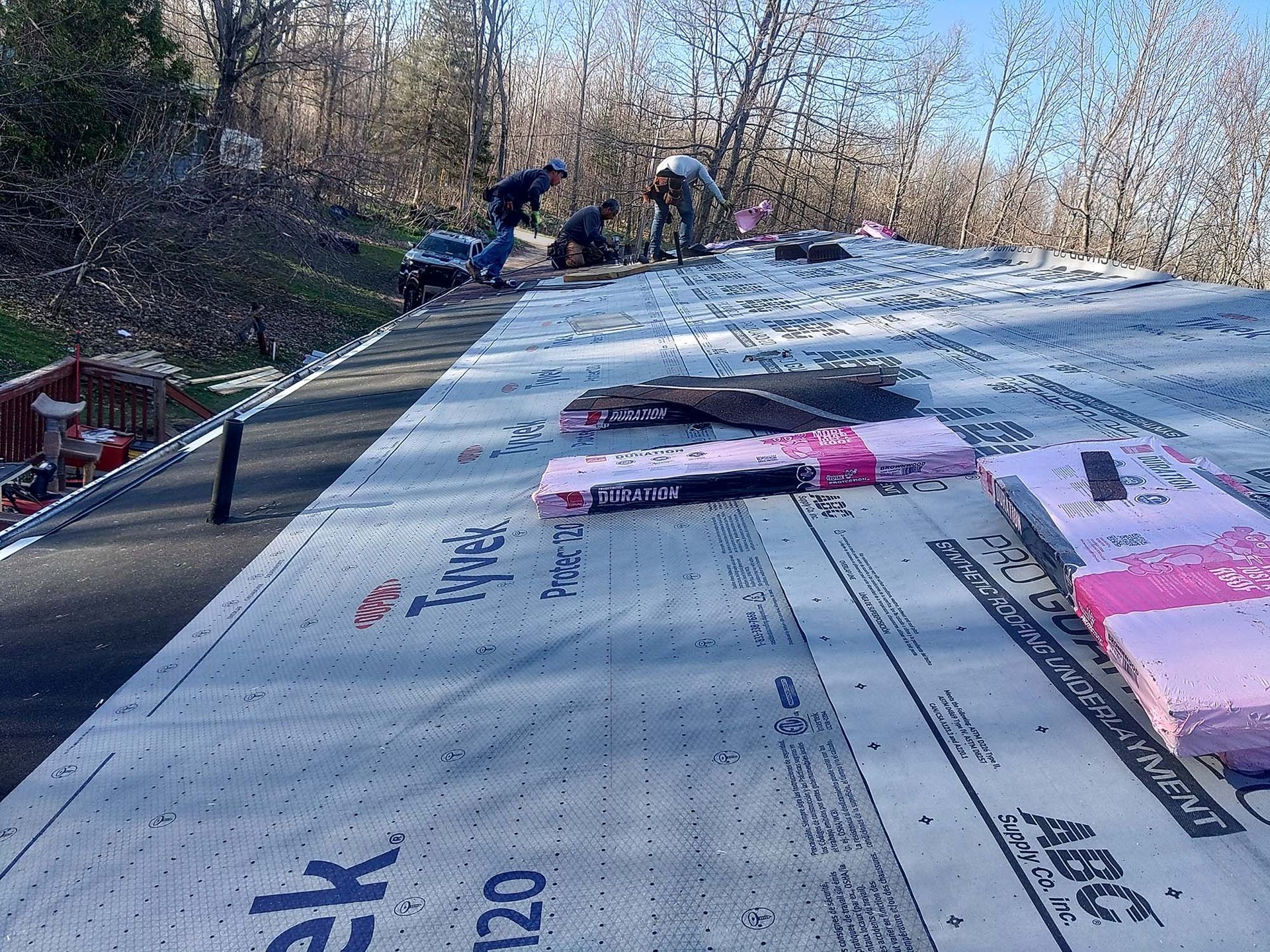 Roofers installing roofing material on a house, sunny outdoor setting.