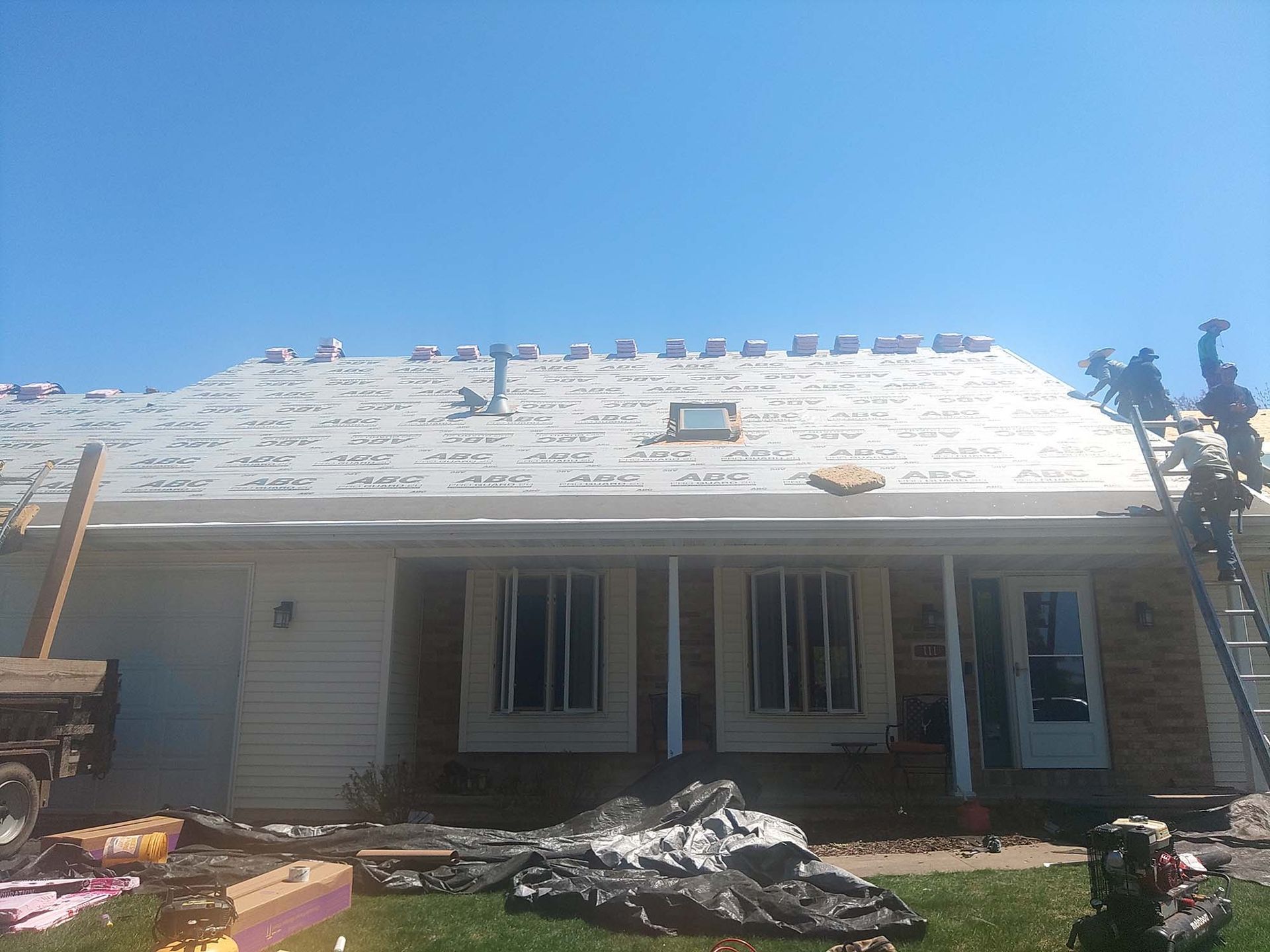 Roof of a house under construction; workers on a ladder, clear blue sky.