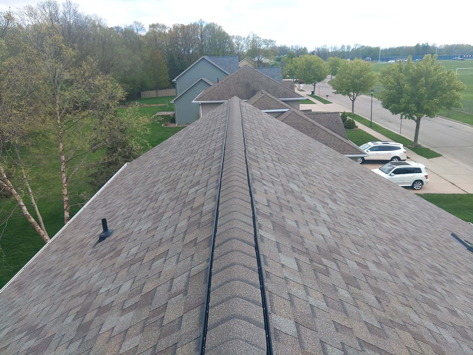 View of a residential rooftop with asphalt shingles, along with a street and trees in the background.