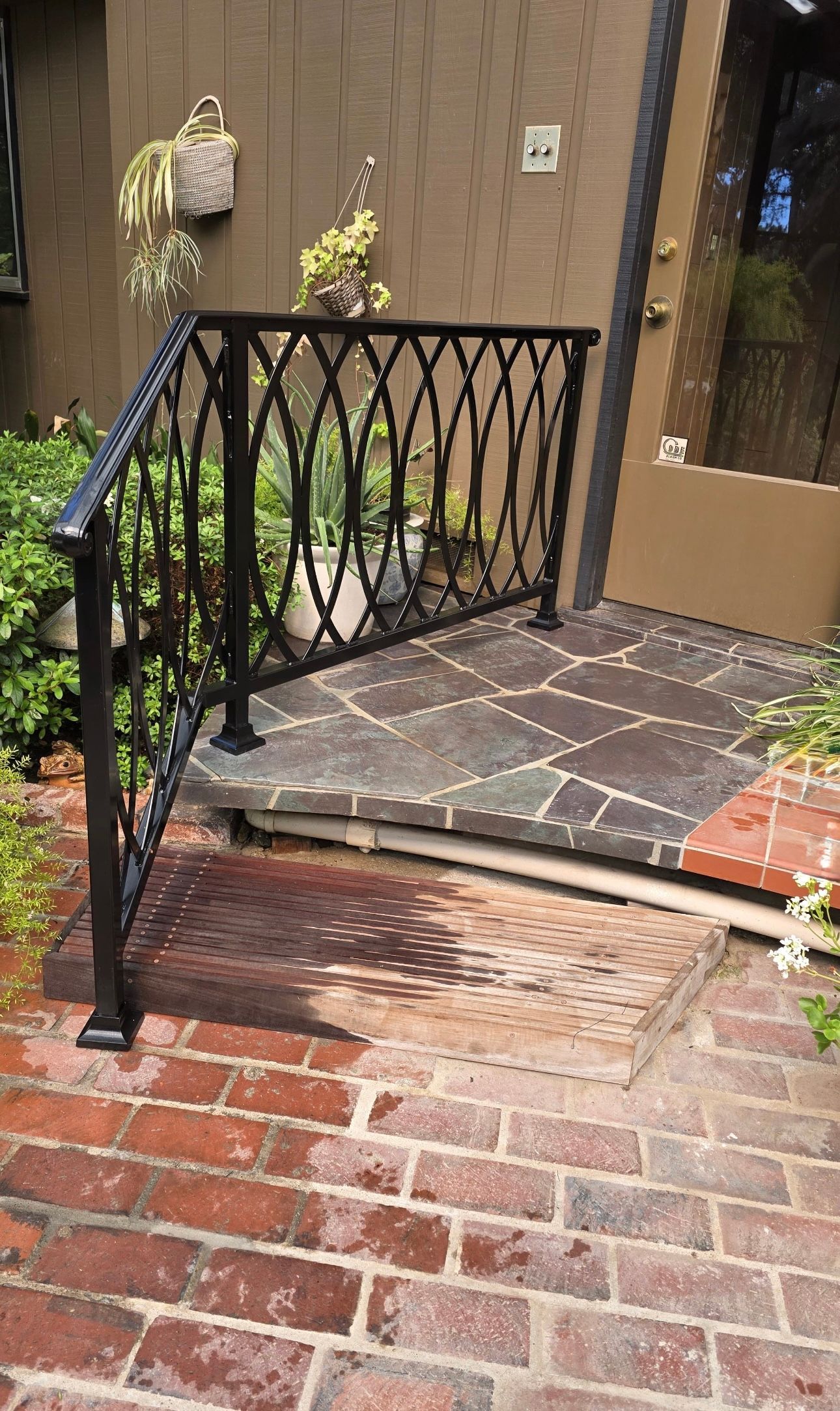 Black iron railing on a brick and stone pathway leading to a doorway.