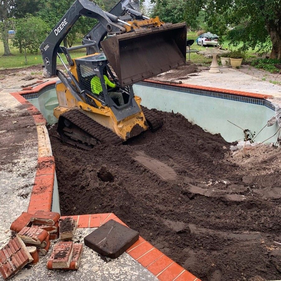 Skid steer removing dirt from a swimming pool during demolition; red brick border.