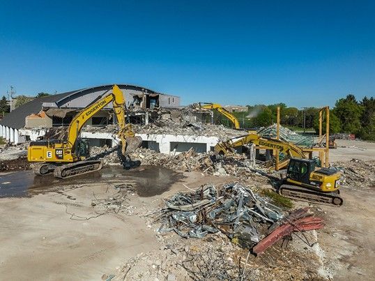 Three yellow excavators demolishing a building under a clear blue sky.