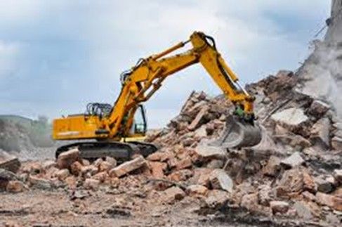 Yellow excavator removing rubble from demolished building.