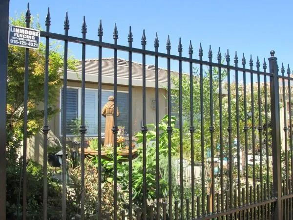 Black wrought-iron fence in front of a house with a statue visible in the yard.