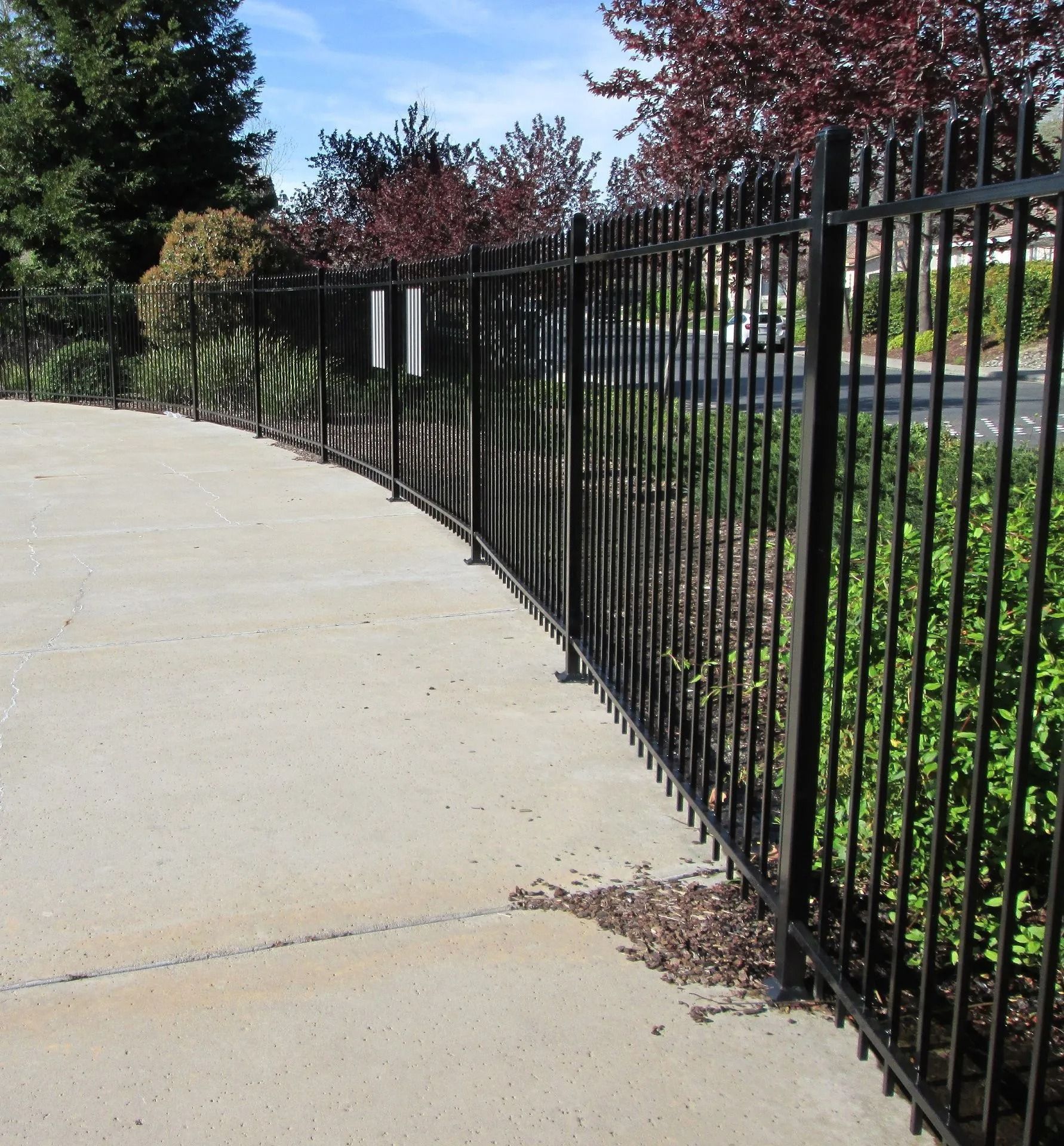 Black metal fence curves along a concrete path, with greenery in the background.