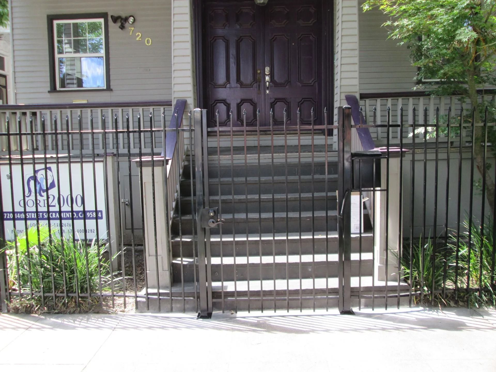 A building entrance with steps, a metal gate, and a sign. The building is gray, and the door is dark wood.