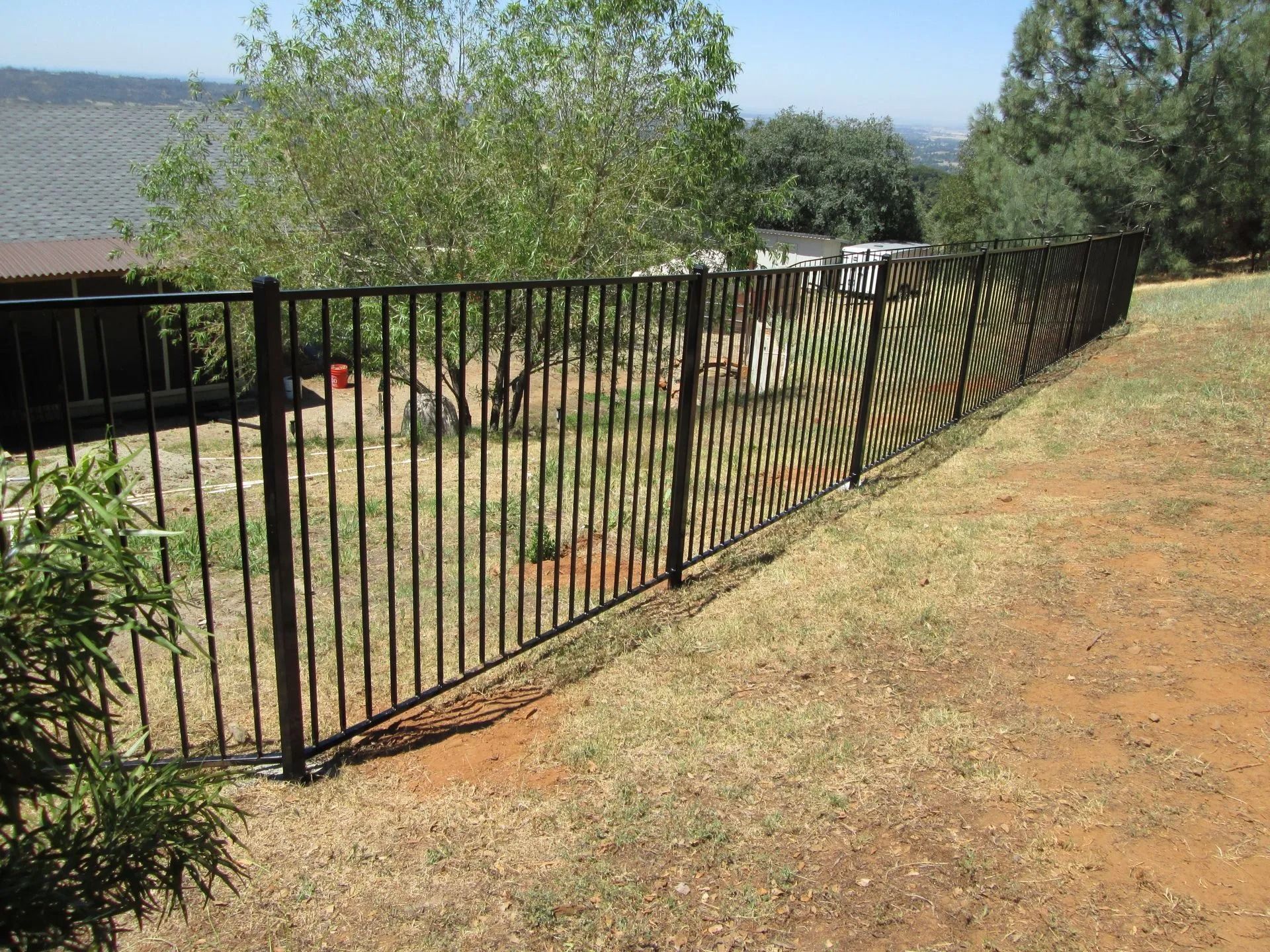 Black metal fence surrounding a yard with grass and trees.