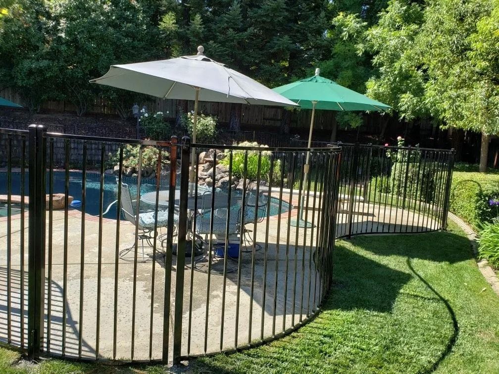 Black fenced-in swimming pool area with patio furniture, two umbrellas on a sunny day.