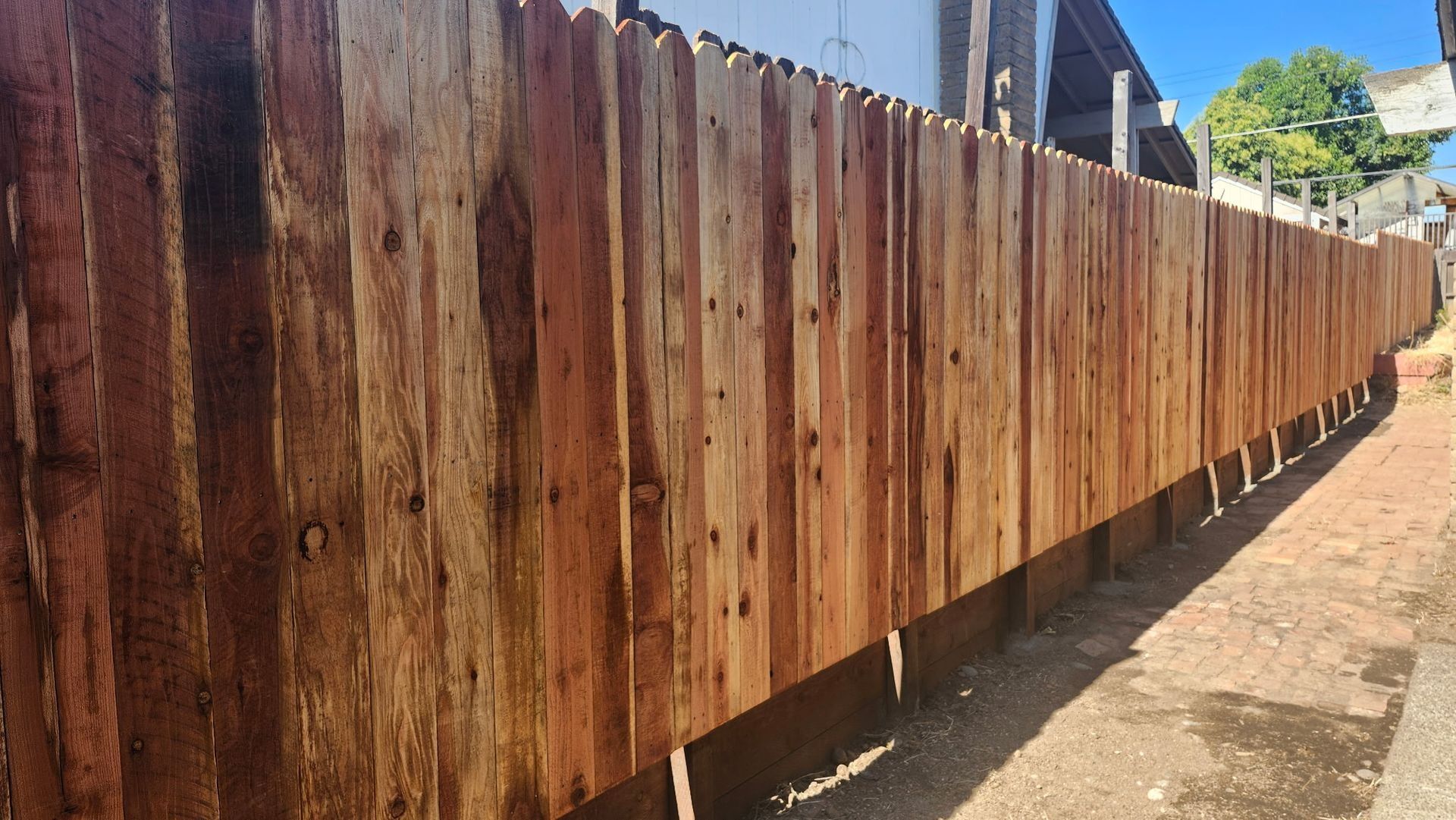 Wooden fence, long and straight, running along a brick pathway on a sunny day.