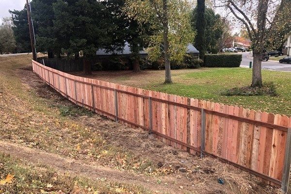 Wooden fence along a grassy area, with trees and houses in the background.