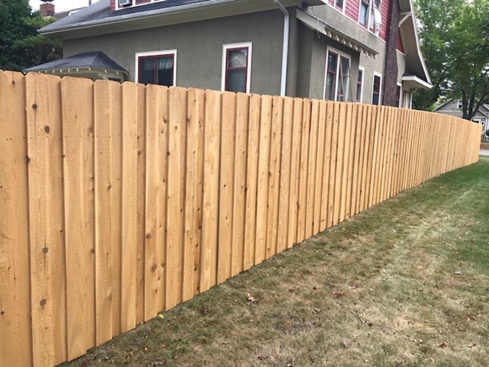 Wooden fence curves along a grassy yard, next to a two-story house with green siding.