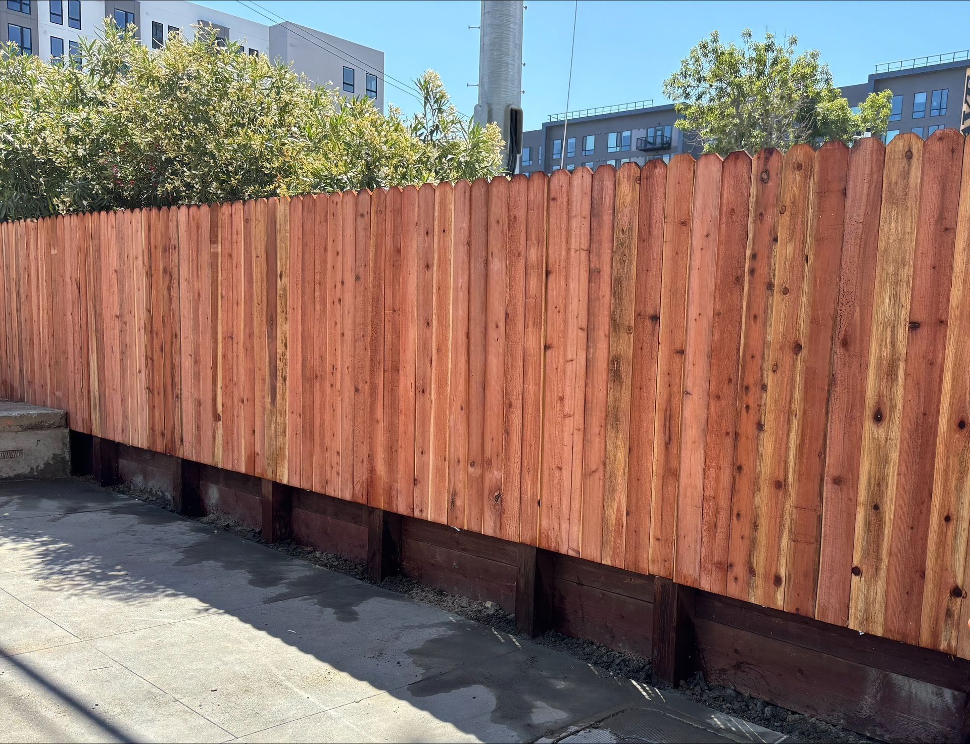 Wooden fence along a paved area; reddish-brown planks on dark brown base.