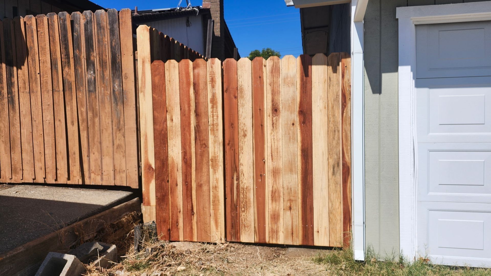 Wooden gate in a backyard, contrasting lighter and darker wood tones against a blue sky.