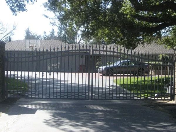 Black metal gate in front of a house. A car is visible on the property, under the trees.