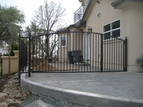 Black metal fence enclosing a concrete patio area near a house with beige walls.