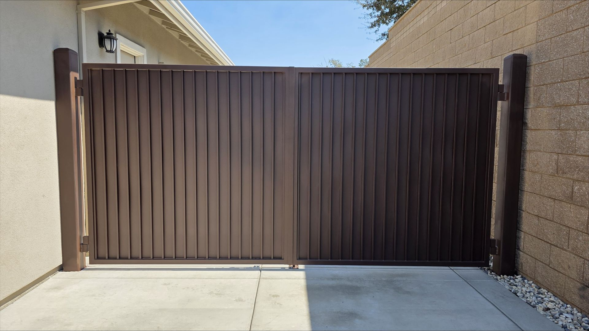 Brown metal gate between walls, likely for a driveway or walkway, with concrete ground.