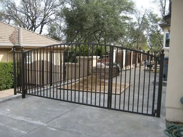 Black iron gate enclosing a driveway, with arched top and vertical bars.