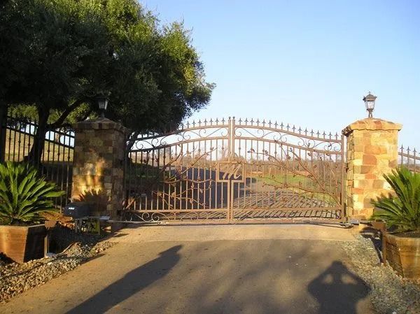 Ornate iron gate, stone pillars, and a driveway leading into a property.