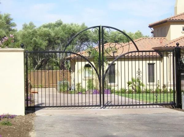 Black wrought-iron driveway gate in front of a tan house.