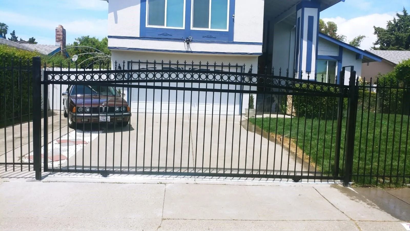 Black iron gate in front of a house. A car is parked behind the gate on a concrete driveway.