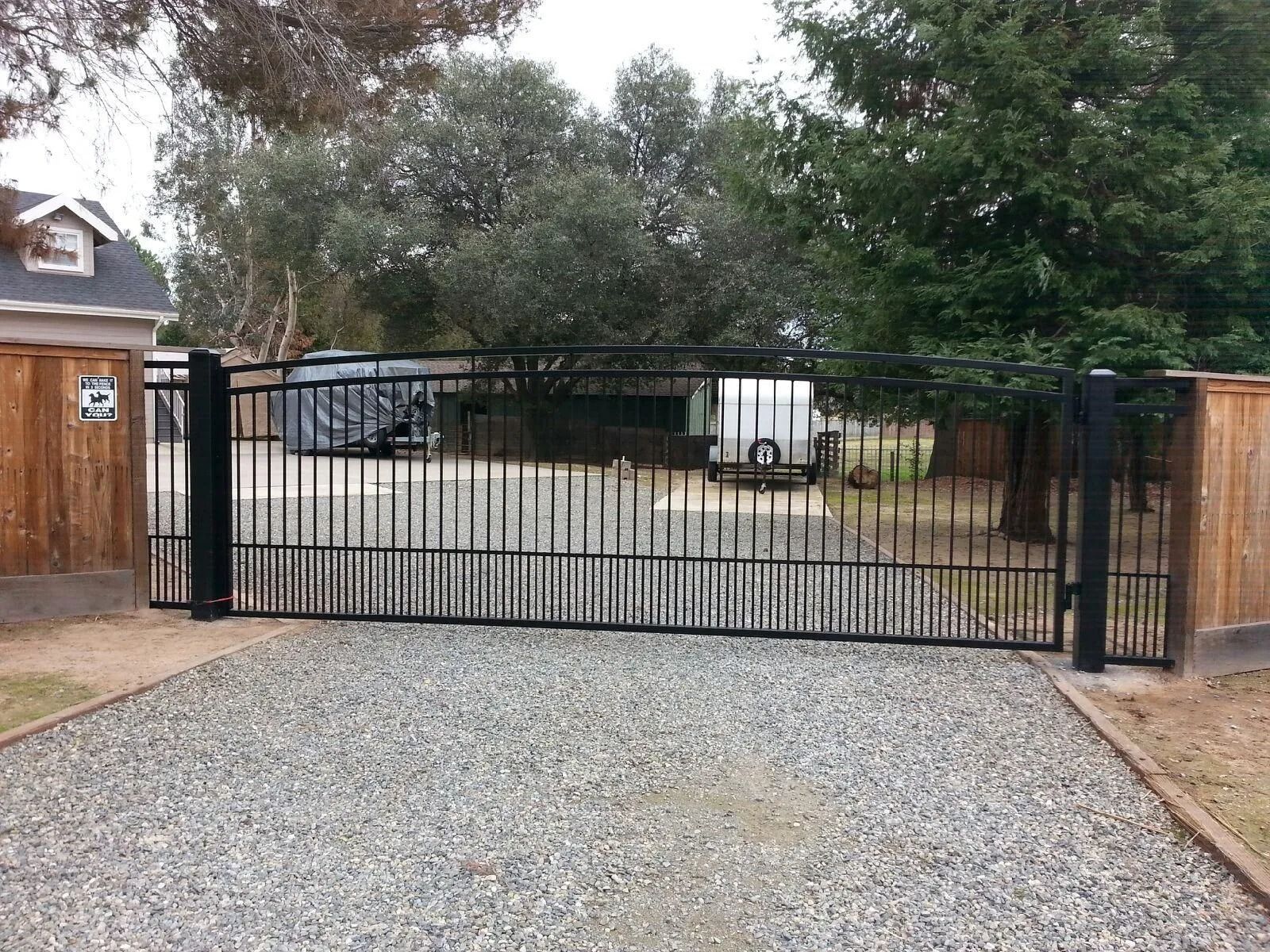 Black metal driveway gate, gravel drive. Wooden fence on either side.