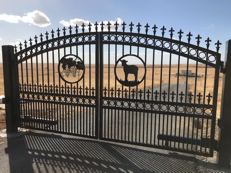 Black metal gate with a sheep and grapes design, set against a desert landscape.