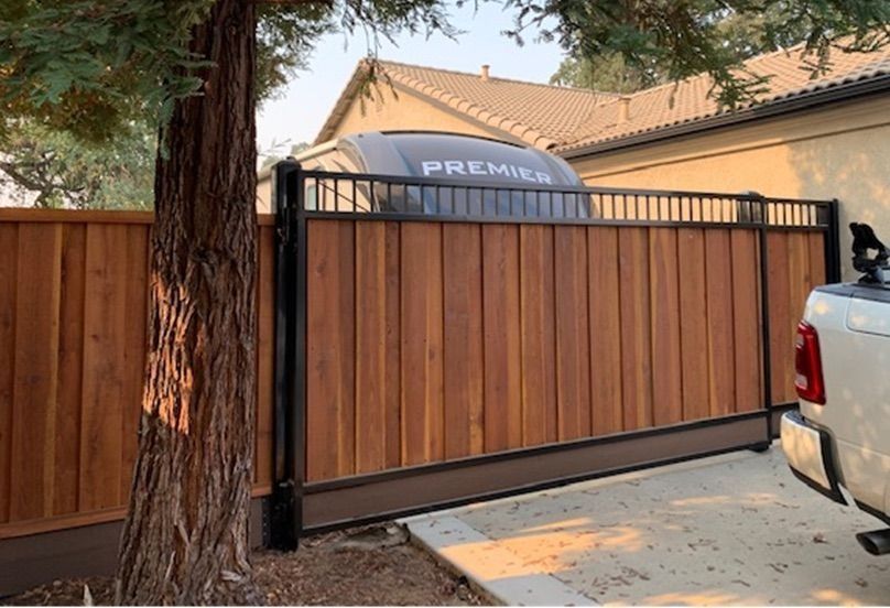 Wooden automatic gate in front of a house, with a Premier trailer behind it and a tree on the left.